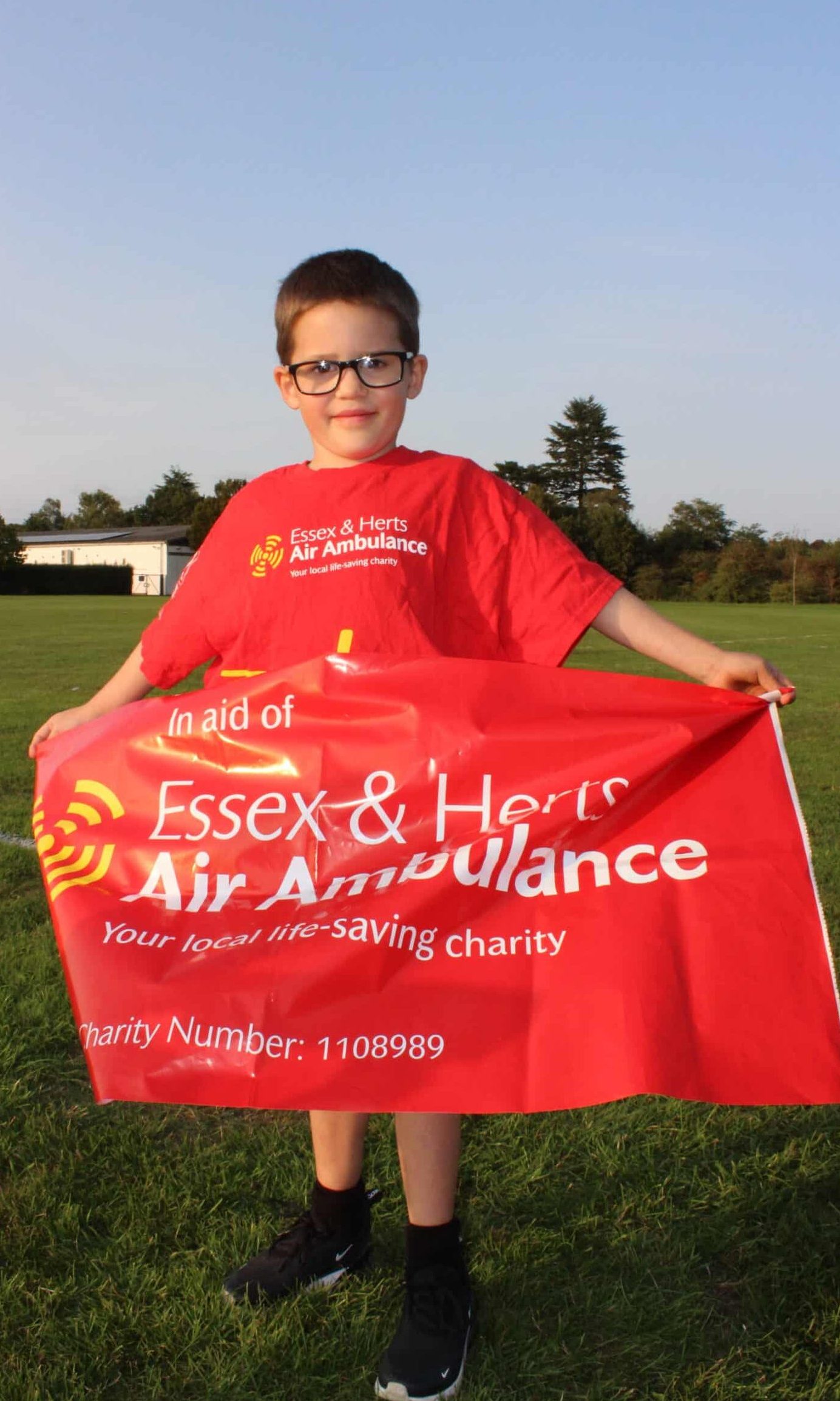 A young boy wearing glasses and a red EHAAT shirt holding up a red banner to fundraise for the charity.