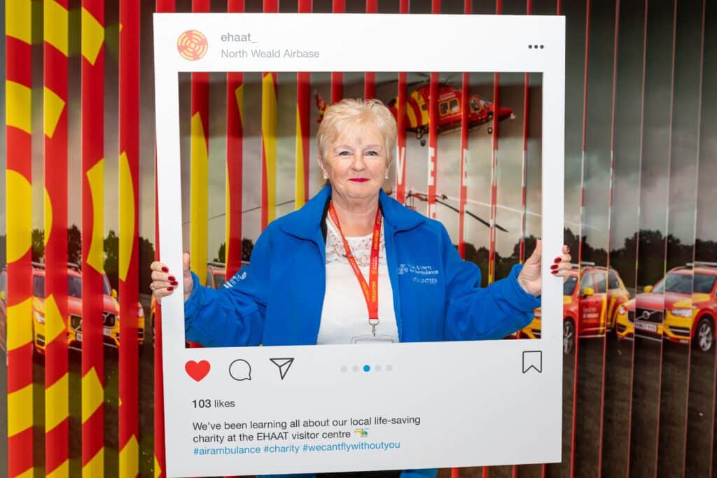 A smiling woman in a blue volunteers fleece holds an instagram frame cutout